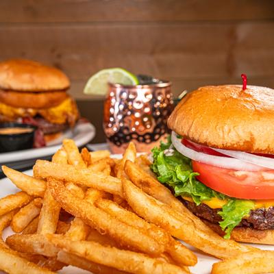 Classic burger with fries alongside cocktail served in a copper mug.