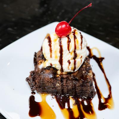 Rocky road brownie topped with ice cream, chocolate drizzle, and a cherry.