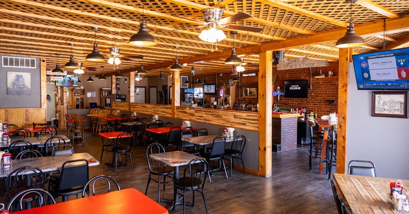 Spacious restaurant interior with wooden beams, various tables, and a bar area
