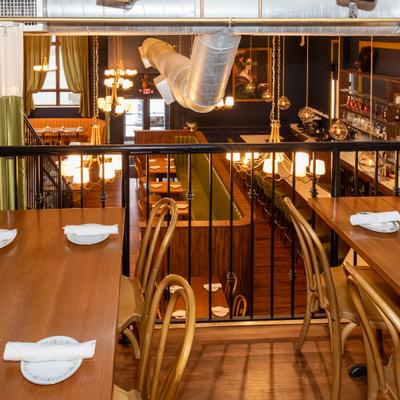 Restaurant mezzanine area overlooking the lower floor with tables, pendant lights, and bar.