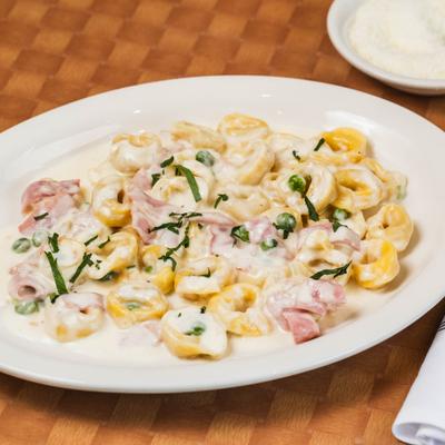 Creamy tortellini pasta with ham and peas, garnished with herbs.