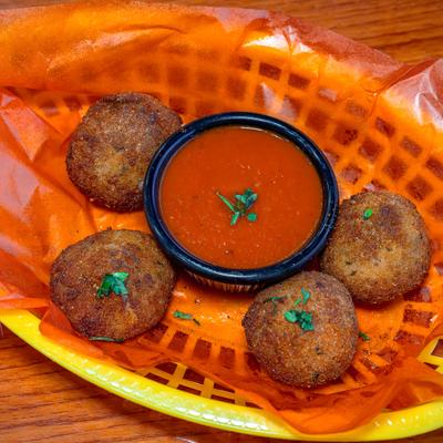 Crispy, golden-brown arancini served in a basket with a side of tomato dipping sauce.