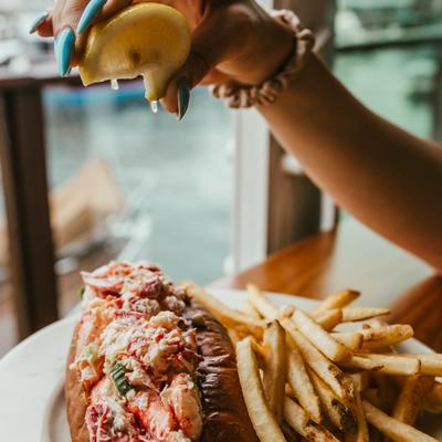 Person squeezing a lemon wedge over the lobster roll with a side of fries.