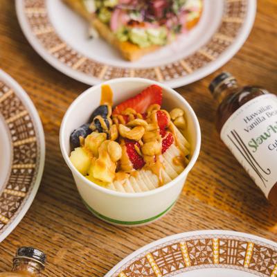 Açaí bowl served alongside a bottle of culinary syrup and avocado toast plates.