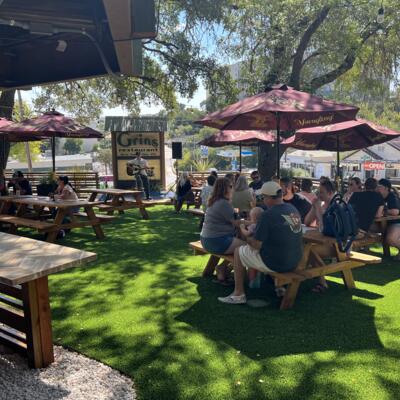 Guests sitting at outdoor picnic tables under umbrellas on a sunny day.