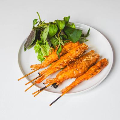 Four fried shrimp skewers served on a white plate with fresh leafy greens.