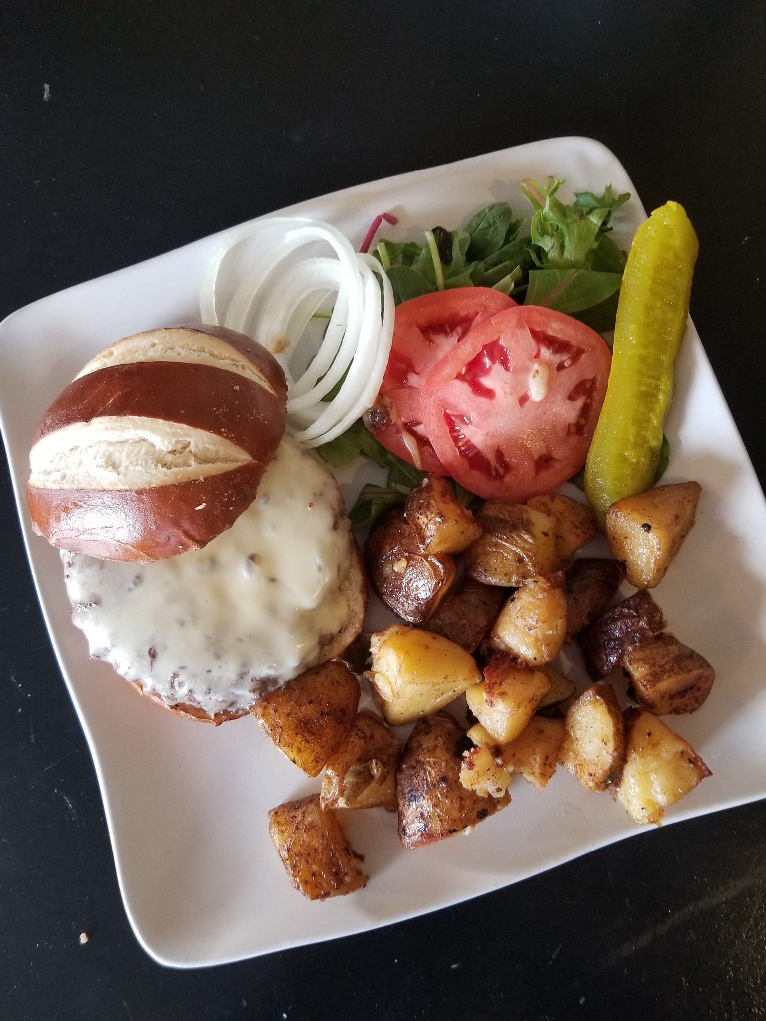 A photo of our burger with cheese and home fried potatoes on a white, square plate