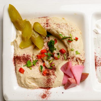 Hummus with spices, pickles, herbs, and pickled radishes.