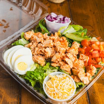 Buffalo Grilled Chicken Salad n a clear plastic container with side cups of toppings.