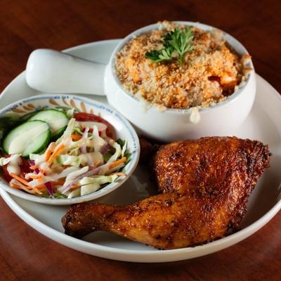A plate with a roasted chicken leg, side salad, and mac and cheese.