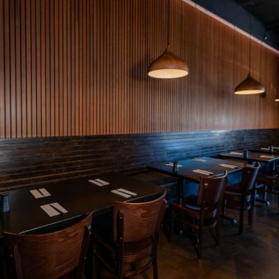 Tables and chairs against a wood-paneled wall under modern pendant lighting.