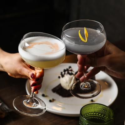 Two hands clinging glasses with cocktails over the table with a dessert.
