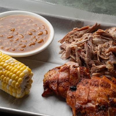 Southern barbecue plate with pulled pork, chicken, corn, and beans.
