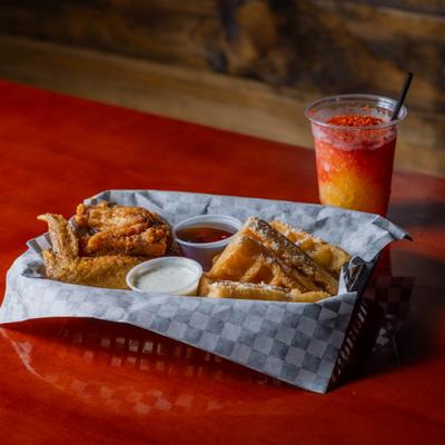 Chicken and waffles with sauces on a red table next to a mangonada.