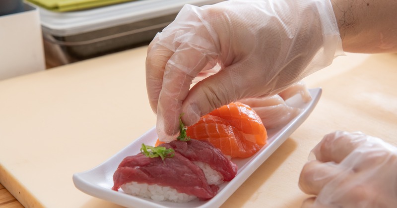 Hands in gloves garnishing nigiri rolls