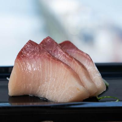 Yellowtail sashimi served on a dark plate.