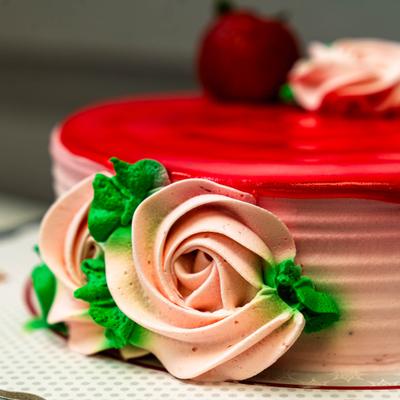 Pink frosted cake topped with red glaze, buttercream roses, and a strawberry.