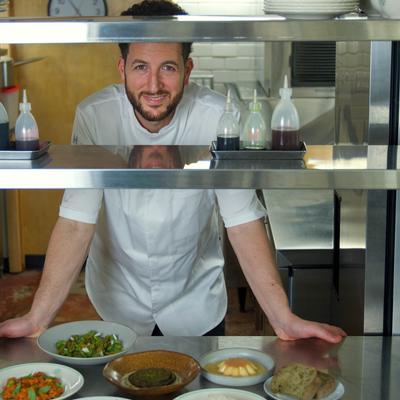 Chef in a commercial kitchen with dishes on a metal shelf.