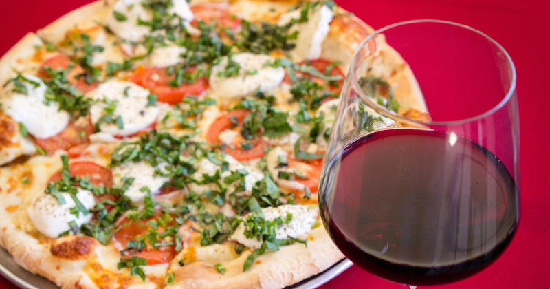 Glass of wine, pizza in the back