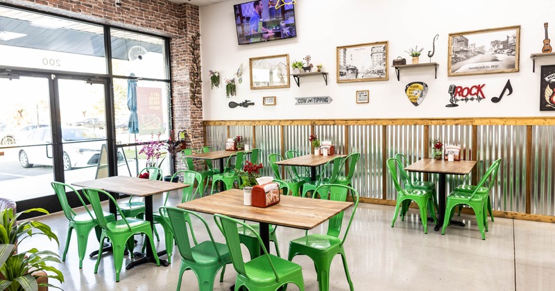 A restaurant interior with green metal chairs, wooden tables, and decorative wall art