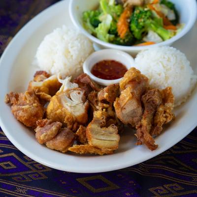 Mixed stir fried vegetables and fried chicken with rice and a sauce.
