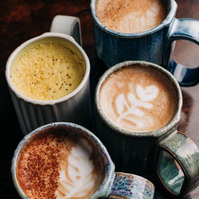 Assorted lattes served in handmade ceramic mugs, top view.