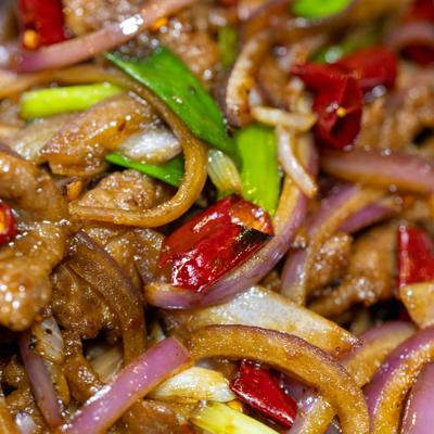 Close-up of spicy stir-fried beef with onions, chilies, and scallions.