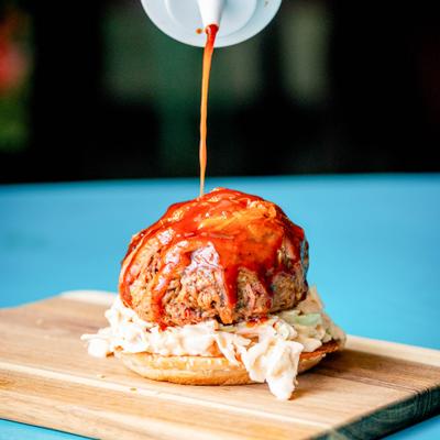 Pulled pork sandwich being topped with BBQ sauce.