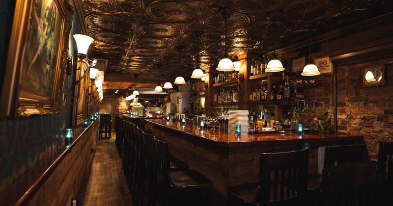 Interior, long bar with bar stools, vintage wallpapers on the wall with paintings on the left