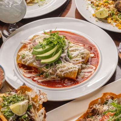Enchiladas covered in red sauce, sour cream, cheese, red onion, and avocado.
