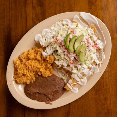 Flautas topped with fresh cheese, crema and avocado accompanied by rice and refried beans.