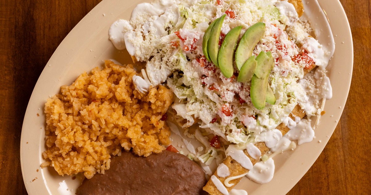Flautas topped with fresh cheese, avocado and crema served with rice and refried beans