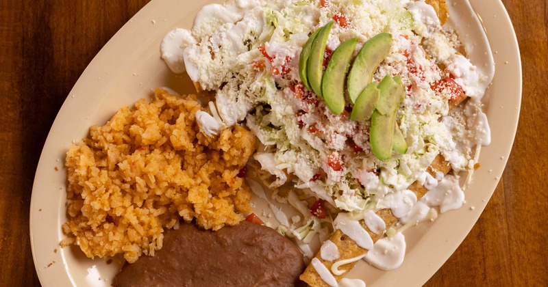 Flautas topped with fresh cheese, avocado and crema served with rice and refried beans