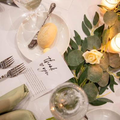 Lit candles and a thank you note with flowers on a beautifully set table, close up top view.