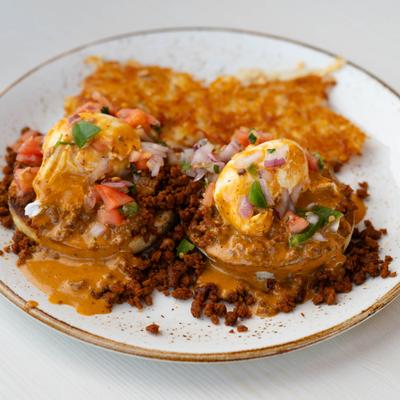 Eggs Benedict topped with chipotle hollandaise sauce and chorizo, served alongside hash browns.