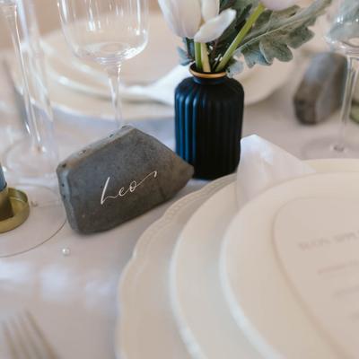 Elegant table setting featuring plates, glasses, a vase of white tulips, and engraved stones.