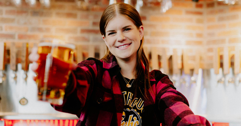 A staff member holding a glass of beer and smiling