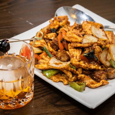 Spicy Basil Chicken served on the table alongside a cocktail.