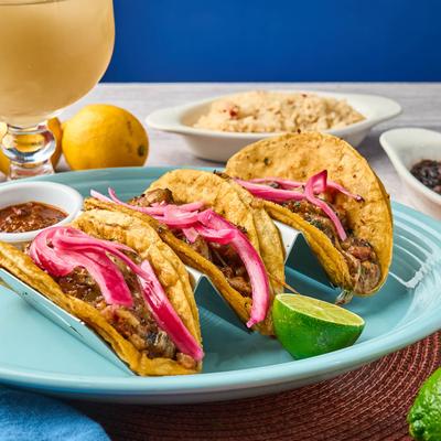 Three tacos with pickled onions and salsa, served with lime, rice, and a drink.