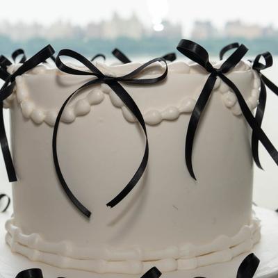 White celebration cake decorated with black ribbon bows.