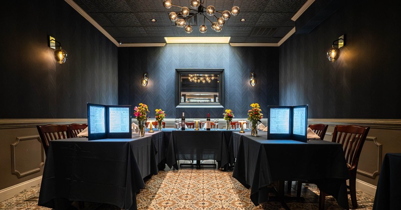 An elegantly set dining room with dark blue walls, a chandelier, patterned floor tiles