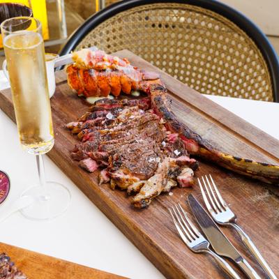 Tomahawk ribeye steak and a grilled lobster tail served on a wooden board.
