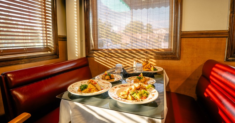 Sunlit restaurant booth with a table covered in plated meals, glasses, and tableware