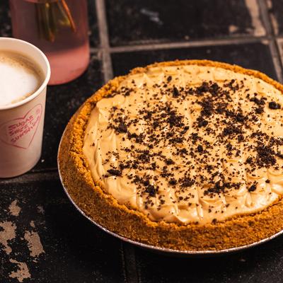 Creamy coffee pie with graham crust topped with chocolate crumbs on dark tile.