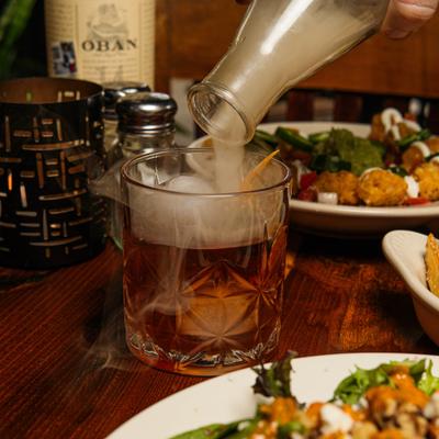 Smoked Old Fashioned being poured from the bottle into a rocks glass.