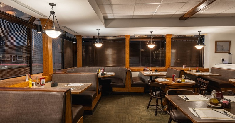 Interior with wooden booths, tables with condiments on them, and pendant lights