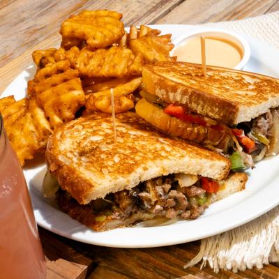 Philly cheesesteak melt served alongside waffle fries and chipotle mayo.