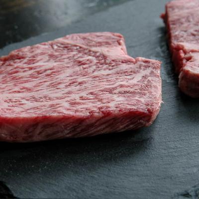 Two uncooked beef pieces placed on a black slate, close up.
