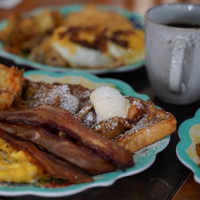 French toast topped with butter and powdered sugar, served with crispy bacon and a coffee.