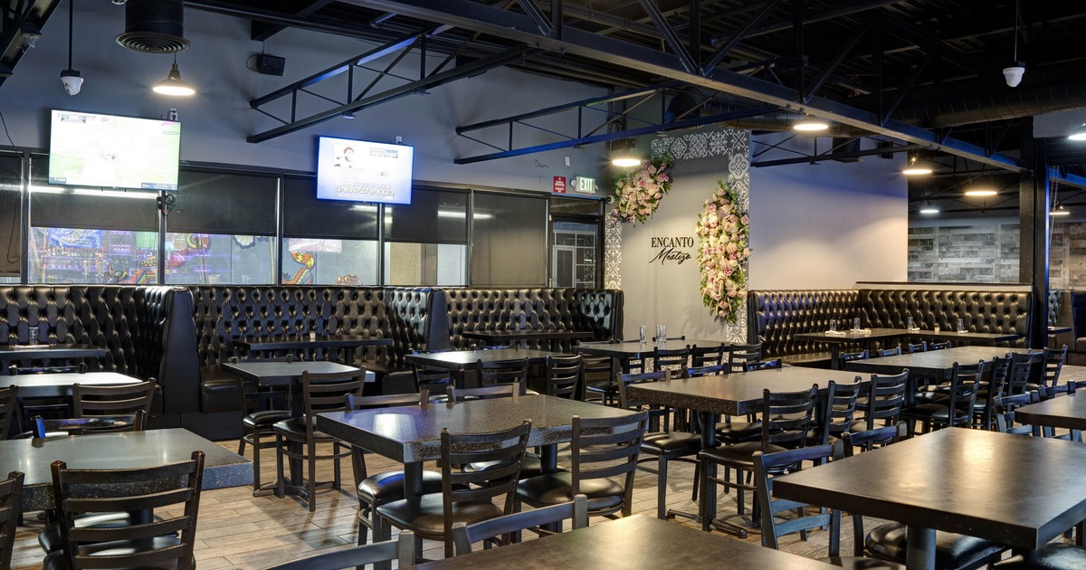 Interior with black tables, chairs and booths, red tiled wall and flat screen TVs